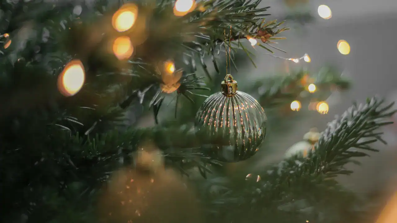 A gold Christmas bauble among evergreen branches and warm fairy lights